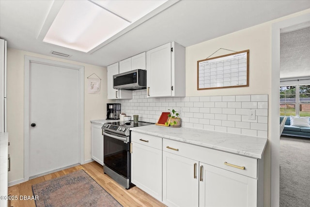 kitchen with light stone countertops, stainless steel appliances, white cabinets, backsplash, and light wood-type flooring