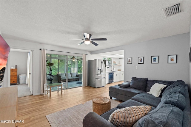 living room featuring visible vents, ceiling fan, a textured ceiling, and light wood finished floors