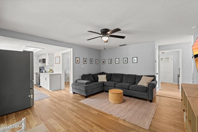 living room featuring visible vents, ceiling fan, a textured ceiling, and light wood-style flooring