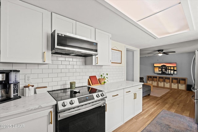 kitchen with light stone countertops, decorative backsplash, light wood-type flooring, white cabinetry, and appliances with stainless steel finishes