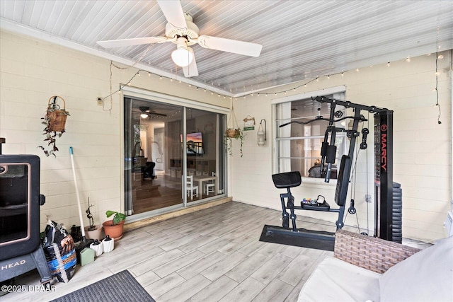 workout room with wood finished floors, ceiling fan, and concrete block wall