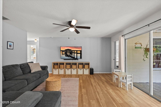 living room with light wood finished floors, a ceiling fan, visible vents, baseboards, and a textured ceiling