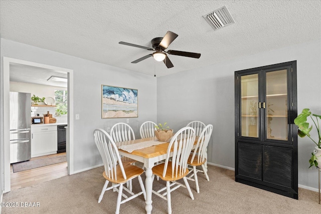 dining room with a ceiling fan, visible vents, light carpet, baseboards, and a textured ceiling
