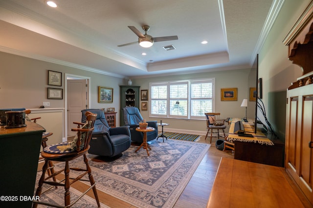 living room with ceiling fan, hardwood / wood-style floors, a tray ceiling, and crown molding