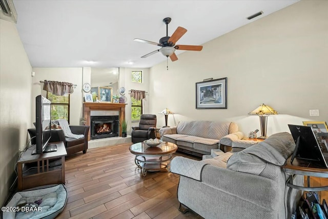 living area with a ceiling fan, visible vents, a lit fireplace, and wood finished floors