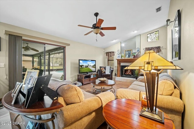 living room featuring lofted ceiling, visible vents, ceiling fan, and a lit fireplace