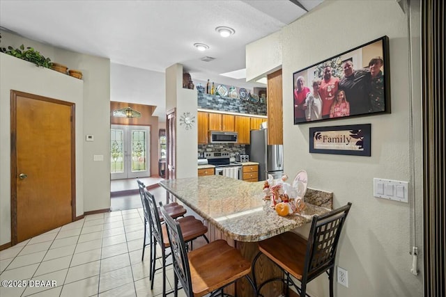 kitchen with a peninsula, french doors, appliances with stainless steel finishes, backsplash, and brown cabinetry