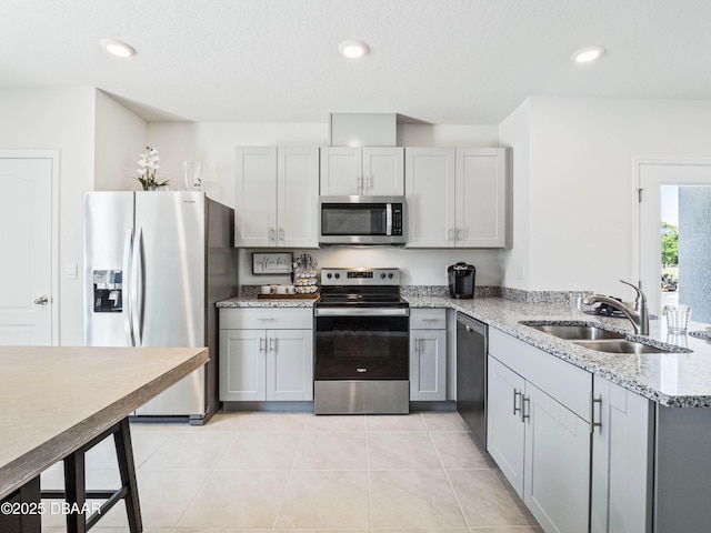 kitchen with gray cabinets, light tile patterned flooring, sink, stainless steel appliances, and light stone countertops