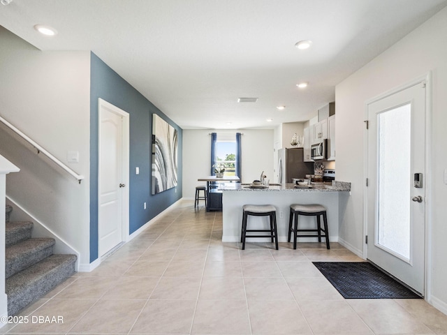 kitchen with light tile patterned floors, a kitchen breakfast bar, kitchen peninsula, stainless steel appliances, and white cabinets