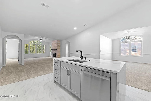 kitchen with light carpet, stainless steel dishwasher, vaulted ceiling, sink, and an island with sink