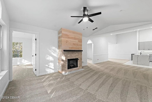 unfurnished living room with light carpet, ceiling fan, lofted ceiling, and a tiled fireplace