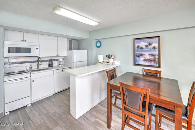 2301 S Atlantic Ave Unit 315, Daytona Beach, FL 32118 - kitchen featuring light hardwood / wood-style floors, kitchen peninsula, sink, white cabinetry, and white appliances