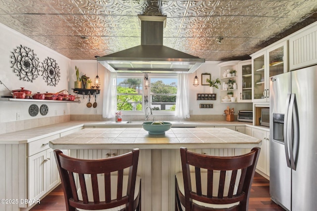 kitchen with wall chimney exhaust hood, an ornate ceiling, open shelves, and stainless steel fridge with ice dispenser