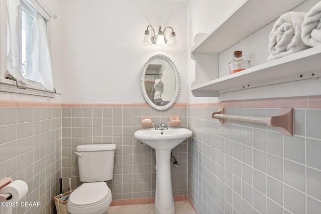 half bath with a wainscoted wall, tile patterned flooring, toilet, and tile walls