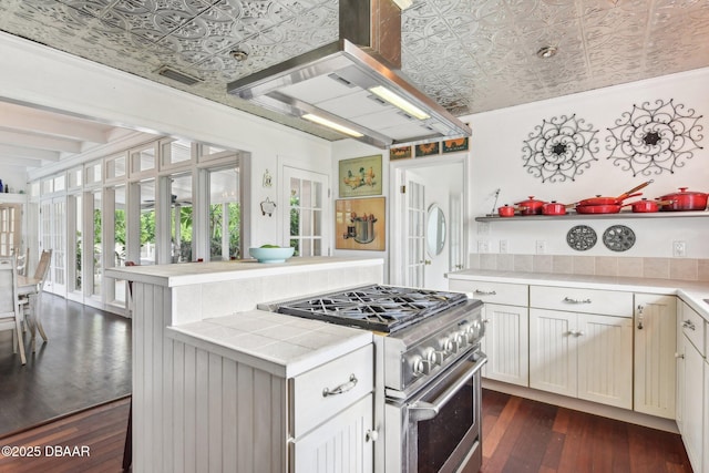 kitchen with tile counters, wall chimney exhaust hood, an ornate ceiling, dark wood-style flooring, and stainless steel stove