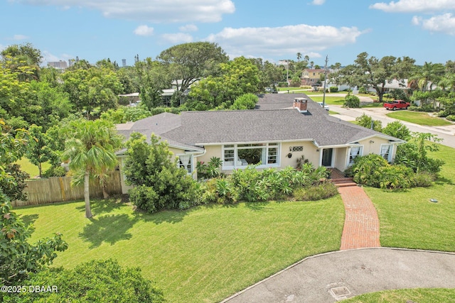 ranch-style home featuring a front lawn, roof with shingles, fence, and stucco siding