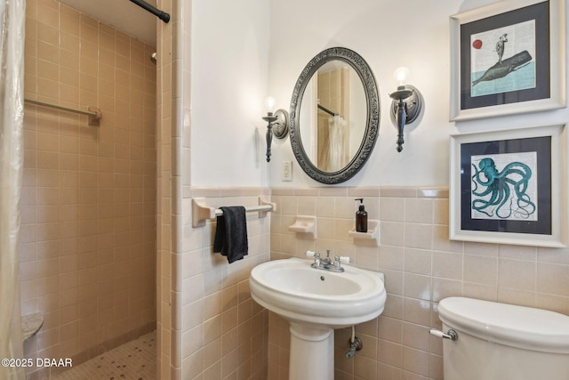 bathroom with toilet, tile walls, tiled shower, and wainscoting