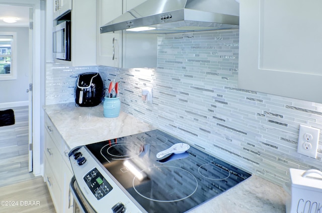 kitchen with backsplash, white cabinetry, wall chimney range hood, and range