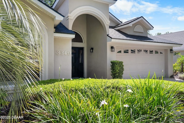 3349 Glenshane Way, Ormond Beach, FL 32174 - view of exterior entry featuring an attached garage, stucco siding, and a shingled roof