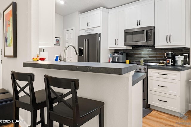 3349 Glenshane Way, Ormond Beach, FL 32174 - kitchen with stainless steel appliances, dark countertops, a breakfast bar area, backsplash, and white cabinets