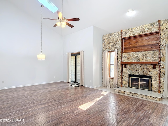 unfurnished living room with ceiling fan, high vaulted ceiling, a stone fireplace, wood finished floors, and baseboards