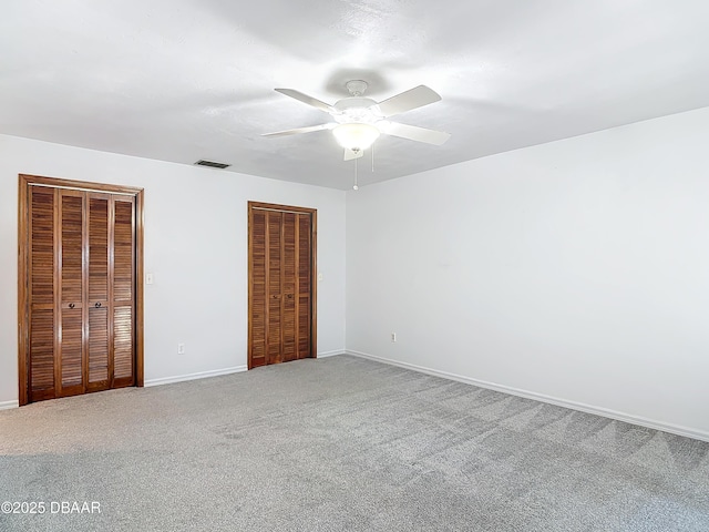 unfurnished bedroom featuring a ceiling fan, visible vents, baseboards, carpet, and two closets