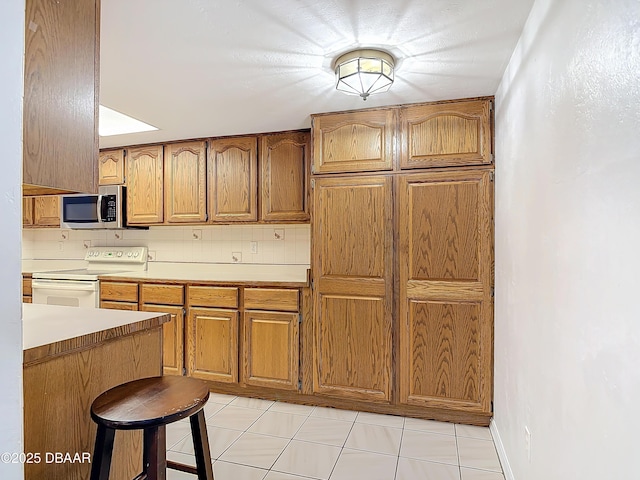 kitchen featuring white electric range, a breakfast bar, light countertops, brown cabinets, and stainless steel microwave