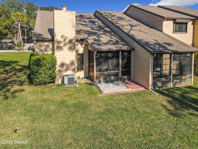 back of property featuring central AC unit, a sunroom, a yard, roof with shingles, and a chimney