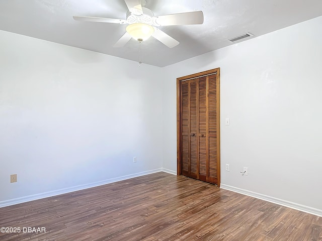 empty room with dark wood-type flooring, visible vents, baseboards, and a ceiling fan