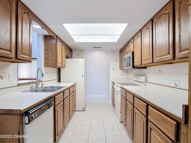 kitchen featuring light countertops, visible vents, brown cabinetry, a sink, and white appliances