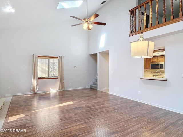 unfurnished living room with ceiling fan, a skylight, wood finished floors, a sink, and stairs