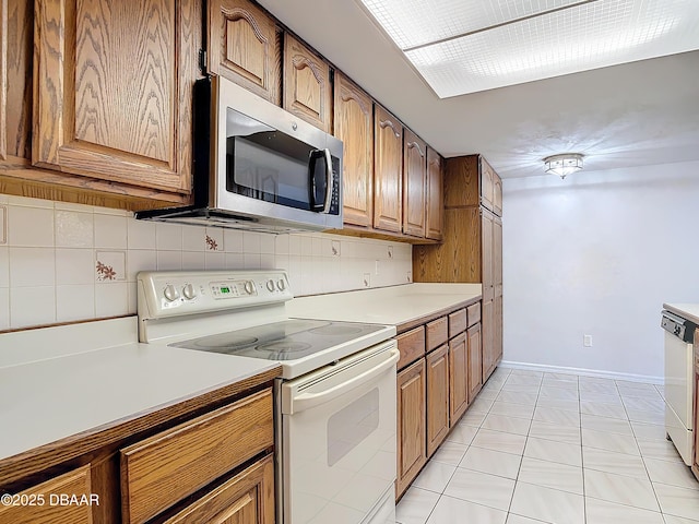 kitchen featuring tasteful backsplash, electric stove, stainless steel microwave, brown cabinets, and light countertops