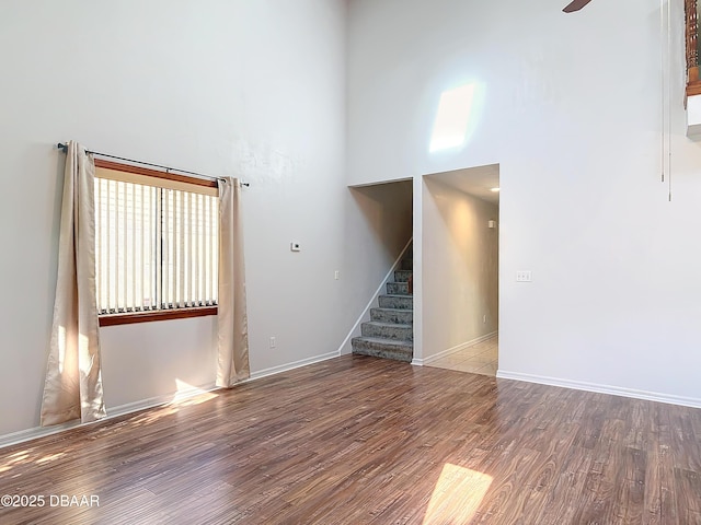 empty room featuring baseboards, stairway, a towering ceiling, and wood finished floors