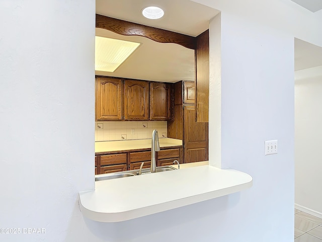 kitchen featuring a sink, baseboards, light countertops, tasteful backsplash, and brown cabinetry