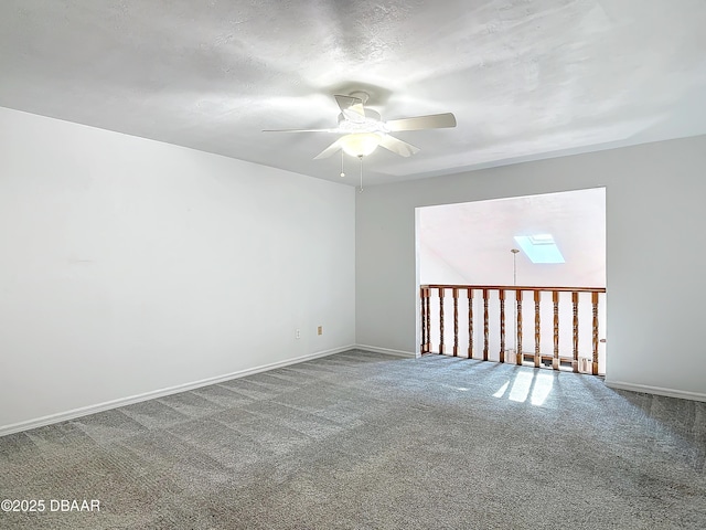 carpeted spare room featuring a skylight, a ceiling fan, and baseboards