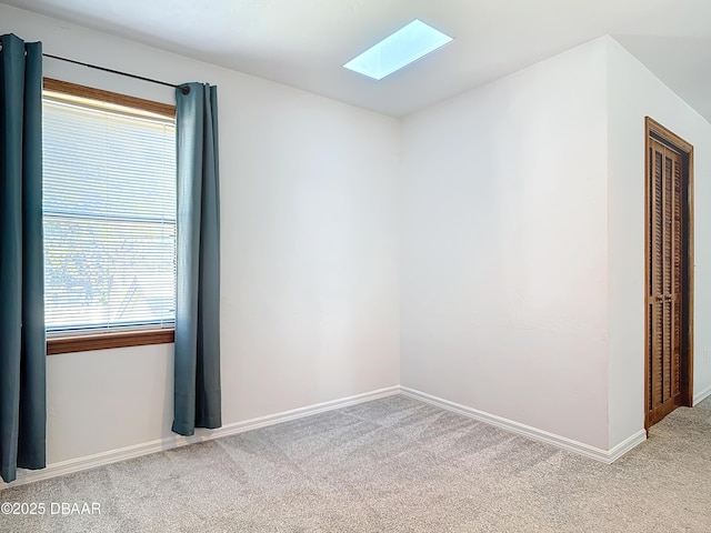 empty room with light carpet, a skylight, and baseboards