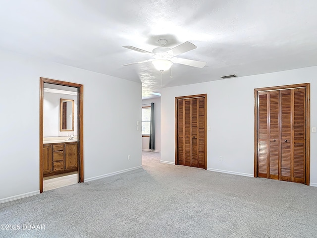 unfurnished bedroom with light carpet, baseboards, visible vents, and multiple closets