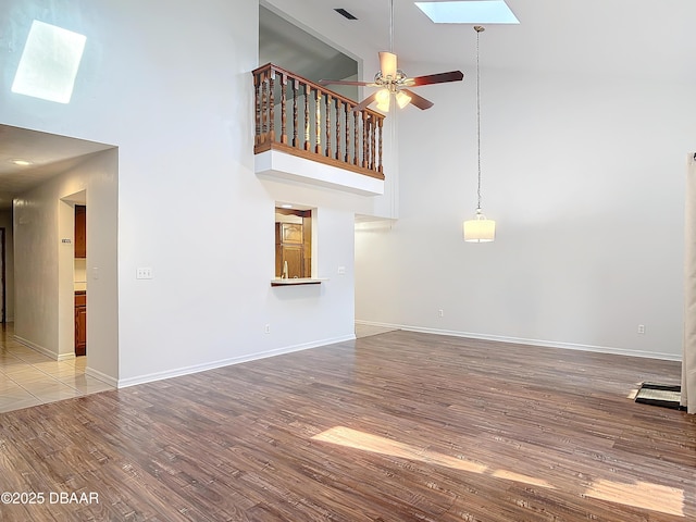 unfurnished living room featuring high vaulted ceiling, a skylight, a ceiling fan, baseboards, and light wood finished floors