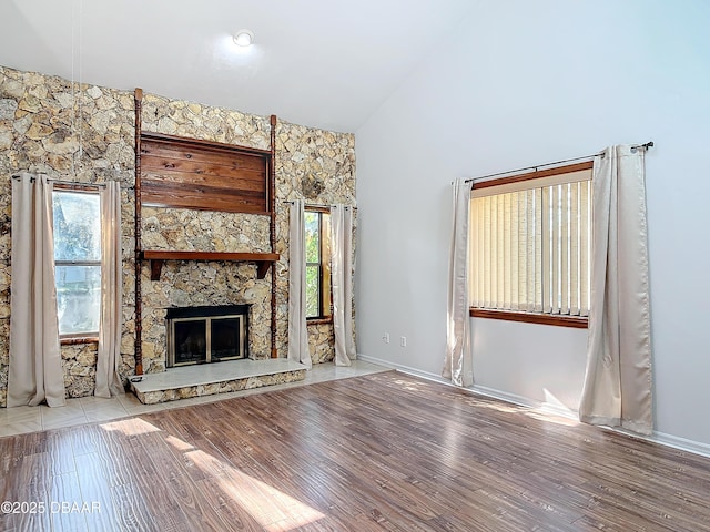 unfurnished living room with high vaulted ceiling, a stone fireplace, and light wood finished floors