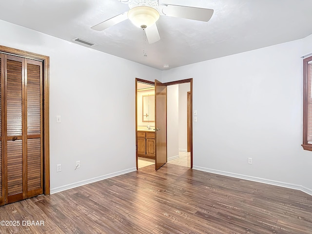 unfurnished bedroom with baseboards, visible vents, ceiling fan, wood finished floors, and a closet