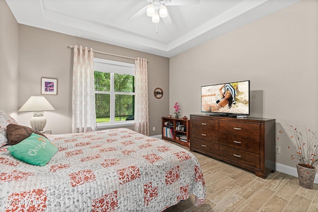 bedroom with ceiling fan, a raised ceiling, and light hardwood / wood-style flooring