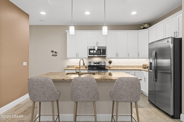 kitchen with appliances with stainless steel finishes, hanging light fixtures, sink, and light hardwood / wood-style flooring