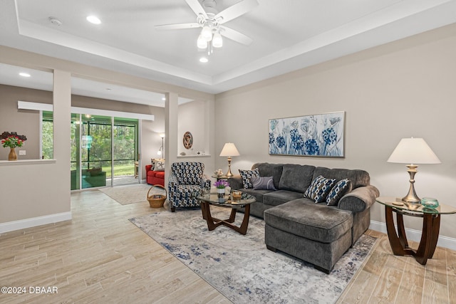 living room with a tray ceiling, ceiling fan, and light hardwood / wood-style flooring