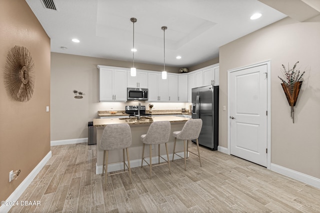 kitchen with stainless steel appliances, hanging light fixtures, light stone countertops, white cabinetry, and light hardwood / wood-style flooring