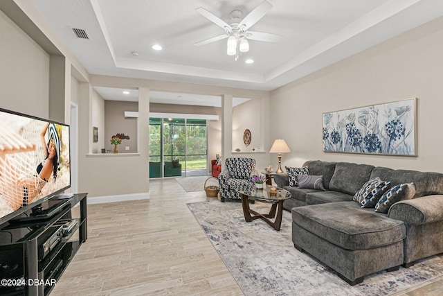 living room featuring ceiling fan, light wood-type flooring, and a tray ceiling