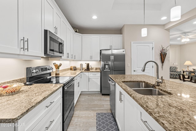 kitchen with hanging light fixtures, sink, white cabinetry, light wood-type flooring, and appliances with stainless steel finishes