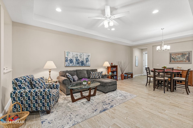 living room featuring light hardwood / wood-style floors, ceiling fan with notable chandelier, and a raised ceiling