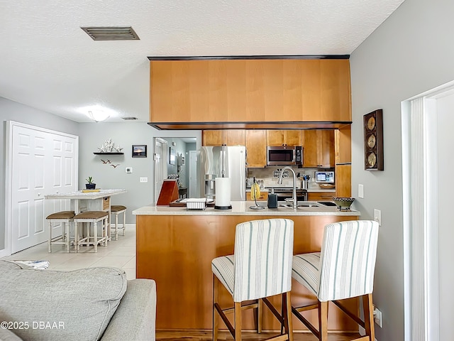 kitchen with a breakfast bar, light tile patterned floors, kitchen peninsula, and appliances with stainless steel finishes