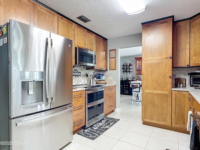 kitchen with a textured ceiling, appliances with stainless steel finishes, light tile patterned flooring, and backsplash