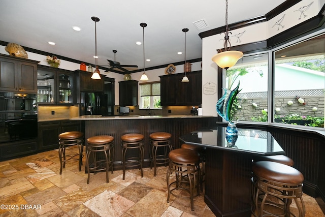 bar featuring decorative light fixtures, sink, black appliances, ceiling fan, and dark brown cabinetry